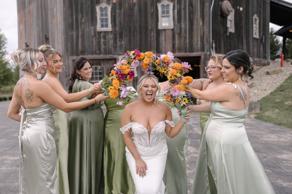 Bride and bridesmaids laughing together in their fall wedding dresses at 1885 Barn in Ohio.