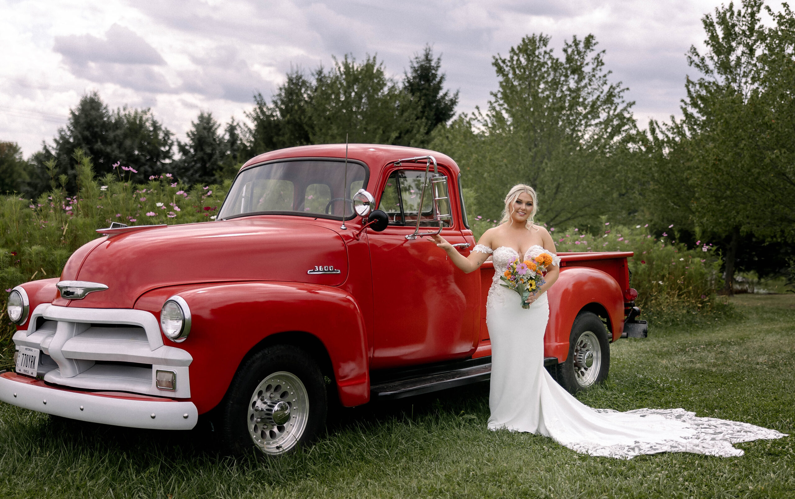 Bride standing beside a vintage red truck holding her bouquet at the 1885 Barn in Ohio, captured by a Cleveland-based wedding photographer.