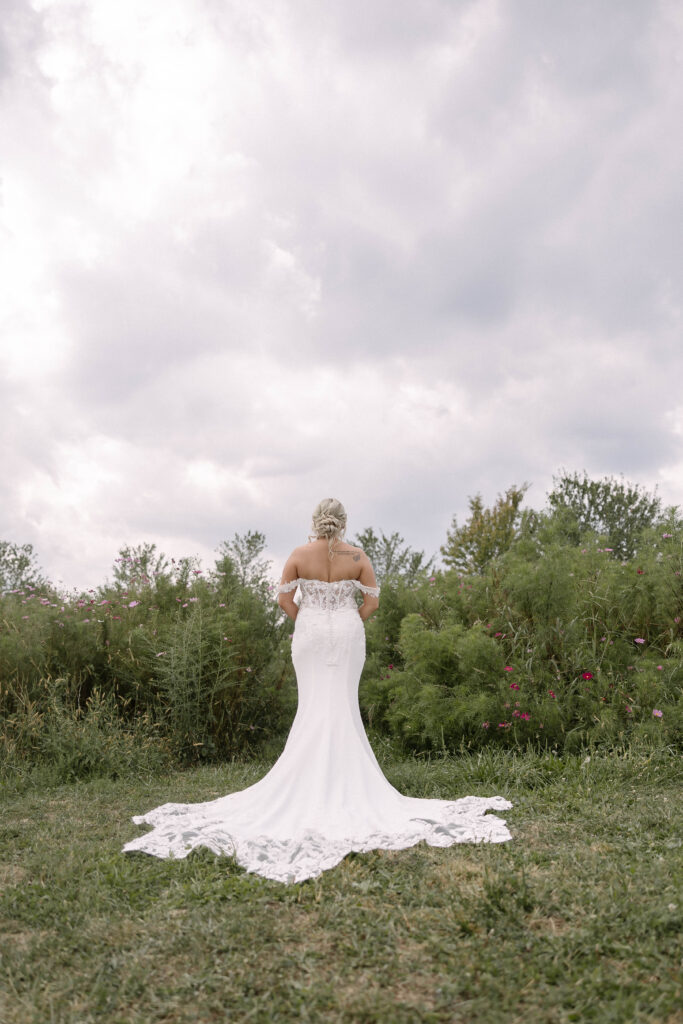 Bride standing in her wedding dress with a long train flowing across the grass at the 1885 Barn in Ohio, photographed by a Cleveland-based wedding photographer.