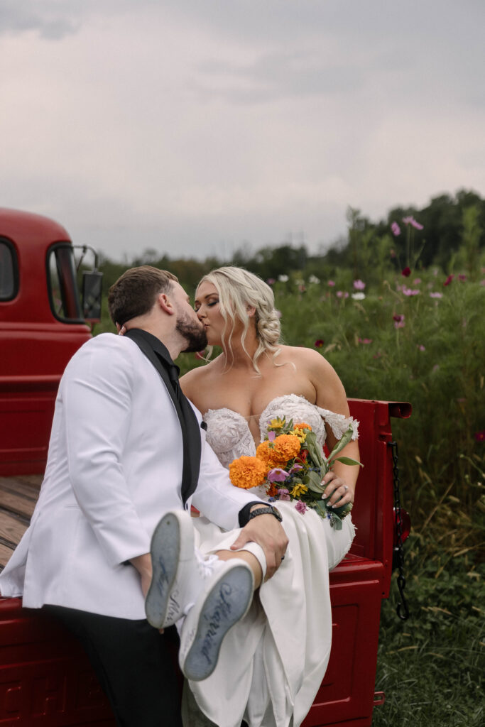 Bride and groom sharing a kiss on the back of a vintage red truck at the 1885 Barn in Ohio during their fall wedding.