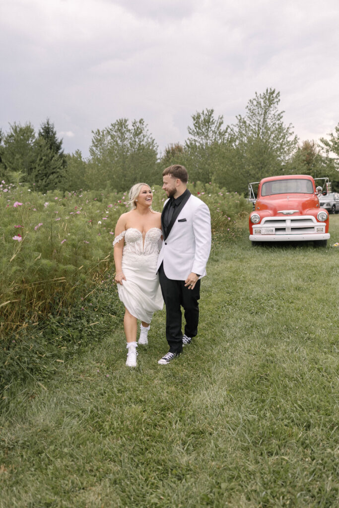 Bride and groom walking hand-in-hand in front of a vintage red truck at the 1885 Barn in Ohio during their fall wedding.