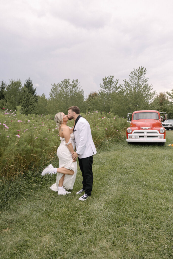 Bride and groom sharing a joyful kiss in front of a vintage red truck at the 1885 Barn in Ohio during their fall wedding.