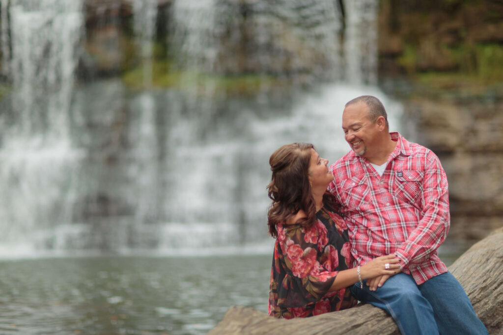 Engaged couple sitting together on a stone ledge in front of the scenic waterfall at Chagrin Falls.