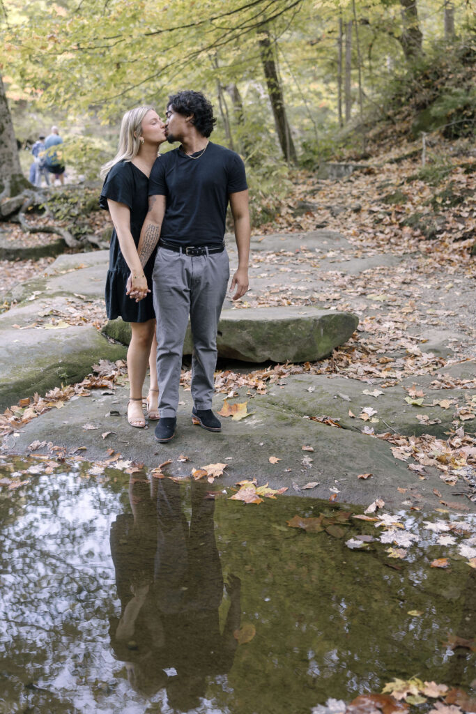 Romantic engagement photo of a couple sitting on a stone ledge by the creek at Grand Pacific Junction in Olmsted Falls