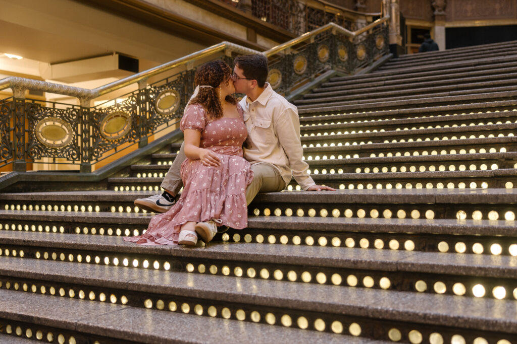 Couple sitting on the illuminated staircase inside the Old Arcade in Cleveland, sharing a romantic moment.