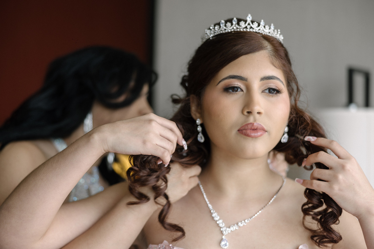 A necklace being fastened around Yariana’s neck before her quinceañera portraits.