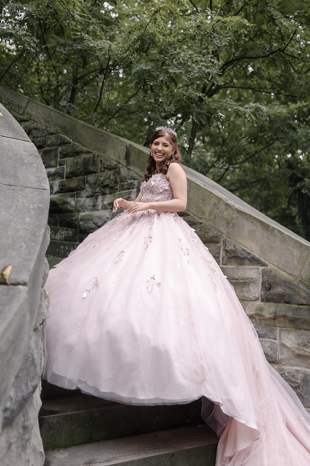 Yariana smiling on a stone staircase with her pink gown arranged across the steps.