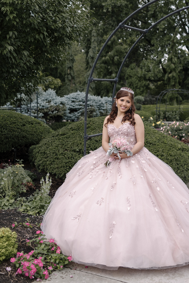 Yariana in her pink quinceañera gown surrounded by flowers and greenery at Cleveland Botanical Garden.
