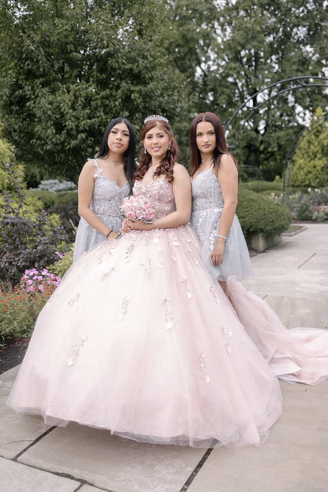 Yariana with two companions in silver dresses on a garden path.
