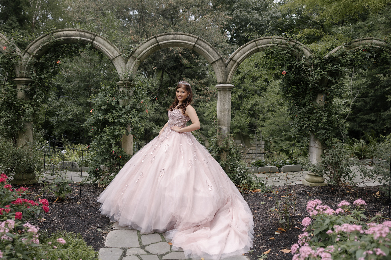 Yariana in her pink quinceañera gown beneath stone arches and flowering greenery at Cleveland Botanical Garden.