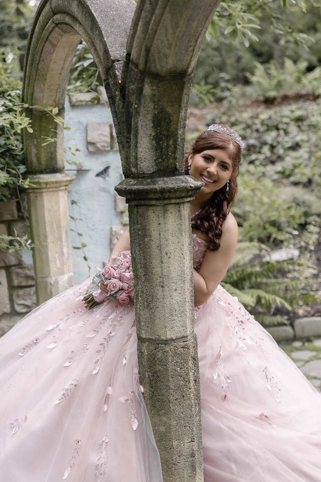 Yariana peeking around a stone column during her quinceañera garden portraits.