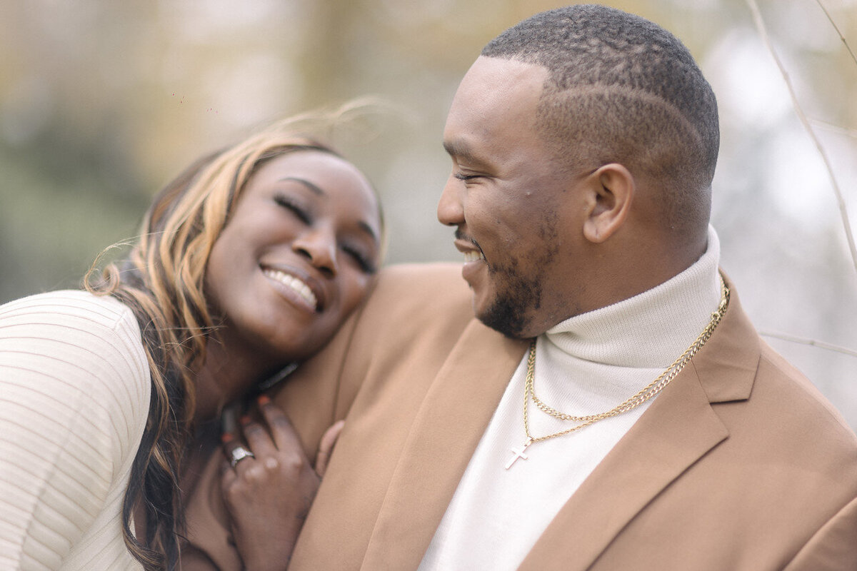 Tanisha and Kevin smiling together in a cream knit dress and camel suit with a cream turtleneck.